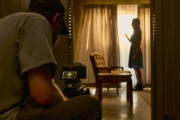 Loş bir odada FX5 kamera kullanan bir videografın, güneş ışığının aydınlattığı bir kişinin siluetini çektiği kullanım görüntüsü.
