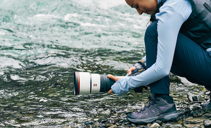 Bir nehir kenarında süper telefoto lensli fotoğraf makinesi kullanan fotoğrafçı