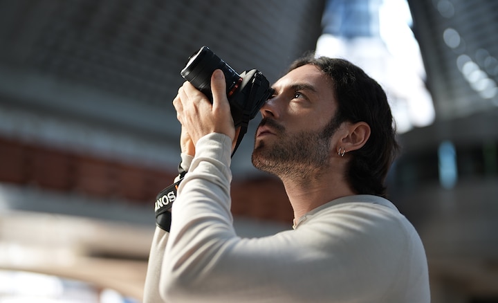 FE 8-14 mm F3.5 Balık gözü G lens takılı bir fotoğraf makinesini tutarak lensin kompakt boyutunu gösteren kişi